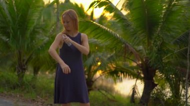 Güzel bir genç kadın bir ANTIMOSQUITO kovucu sprey derisinin üzerinde uygulama Superslowmotion vurdu. Tropikal bir arka plan. Sivrisinek savunma kavramı