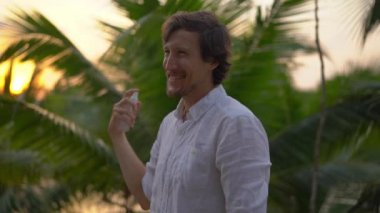 Genç bir adamın derisinde bir ANTIMOSQUITO kovucu sprey uygulama Superslowmotion atış. Tropikal bir arka plan. Sivrisinek savunma kavramı