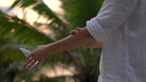 Superslowmotion shot of a young man applying an antimosquito repellent spray on his skin. A tropical background. Mosquito defense concept — Stock Video