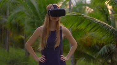 Güzel bir genç kadın portre çekim tropikal bir parkta bir Vr kulaklık kullanın. Tropik bölgelerde biriymiş gibi vr gözlük takan bir kişi geliyor. Artırılmış gerçeklik kavramı