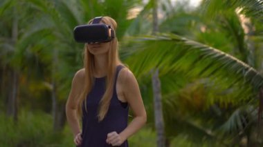 Güzel bir genç kadın portre çekim tropikal bir parkta bir Vr kulaklık kullanın. Tropik bölgelerde biriymiş gibi vr gözlük takan bir kişi geliyor. Artırılmış gerçeklik kavramı