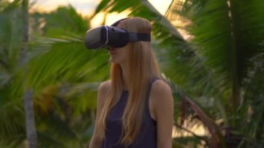 Güzel bir genç kadın portre çekim tropikal bir parkta bir Vr kulaklık kullanın. Tropik bölgelerde biriymiş gibi vr gözlük takan bir kişi geliyor. Artırılmış gerçeklik kavramı