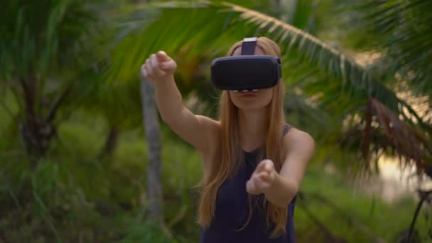 Close-up shot van een mooie jonge vrouw een Vr-headset gebruiken in een tropisch park. Een persoon met een vr bril voelt alsof hij in de tropen is. Augmented reality concept — Stockvideo