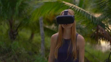 Güzel bir genç kadın portre çekim tropikal bir parkta bir Vr kulaklık kullanın. Tropik bölgelerde biriymiş gibi vr gözlük takan bir kişi geliyor. Artırılmış gerçeklik kavramı