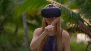 Güzel bir genç kadın portre çekim tropikal bir parkta bir Vr kulaklık kullanın. Tropik bölgelerde biriymiş gibi vr gözlük takan bir kişi geliyor. Artırılmış gerçeklik kavramı