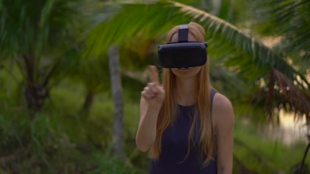 Primer plano de una hermosa joven que usa un casco VR en un parque tropical. Una persona que usa anteojos vr se siente como si estuviera en el trópico. Concepto de realidad aumentada — Vídeos de Stock