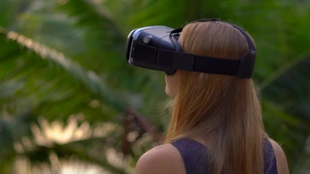 Gros plan d'une belle jeune femme utilisant un casque VR dans un parc tropical. Une personne portant des lunettes vr a l'impression d'être sous les tropiques. Concept de réalité augmentée — Video