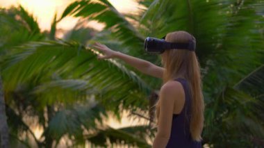 Güzel bir genç kadın portre çekim tropikal bir parkta bir Vr kulaklık kullanın. Tropik bölgelerde biriymiş gibi vr gözlük takan bir kişi geliyor. Artırılmış gerçeklik kavramı