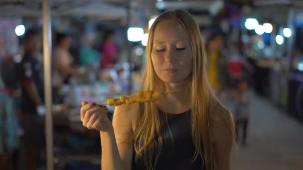 Closeup πλάνο του μια όμορφη νεαρή γυναίκα τρώει squeed ένα μπάρμπεκιου σε μια ασιατική νυχτερινή αγορά. Travell στην Ασία έννοια. Έννοια των ασιατικών τροφίμων — Αρχείο Βίντεο