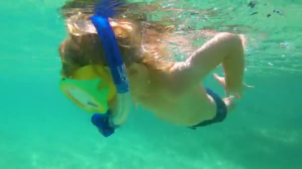 4k tiro subaquático de um menino bonito snorkeling com uma máscara e tubo em um mar tropical com muitos peixes tropicais ao seu redor — Vídeo de Stock