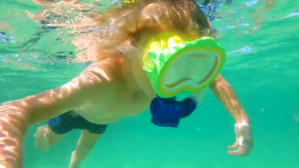 4k inyección submarina de un niño lindo buceando con una máscara y tubo en un mar tropical con un montón de peces tropicales que lo rodean — Vídeo de stock