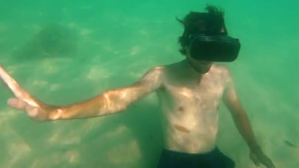 Prise de vue sous-marine d'un jeune homme utilisant un casque VR posé sur un fond marin. Une personne portant des lunettes vr se sent comme il est dans une mer tropicale. Concept de réalité augmentée — Video