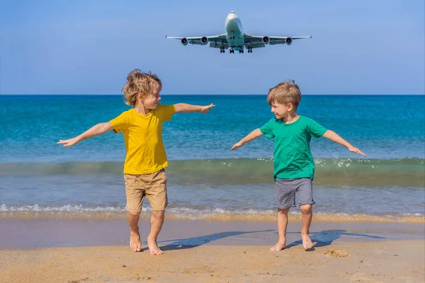 Due ragazzi felici si divertono sulla spiaggia a guardare gli aerei di atterraggio. Viaggiare su un aereo con il concetto di bambini. Spazio di testo. Island Phuket in Thailandia. Un paradiso impressionante. Spiaggia calda Mai Khao. Incredibile. — Foto Stock