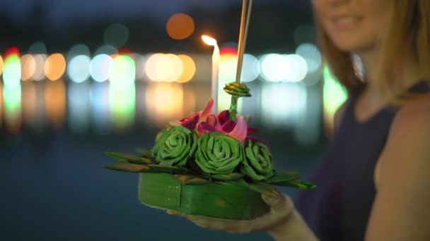 Fotografía en cámara lenta de una hermosa joven que enciende una vela sosteniendo un krathong en sus manos celebrando una fiesta de Loi Krathong en Tailandia — Vídeos de Stock