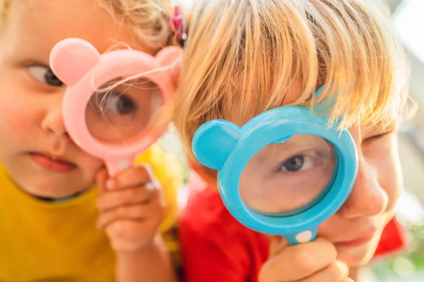 Niño y niña están mirando en una lupa contra el fondo del jardín. Educación en el hogar — Foto de Stock