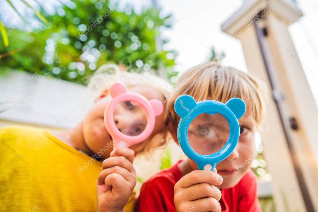 Boy and girl are looking in a magnifying glass against the background of the garden. Home schooling