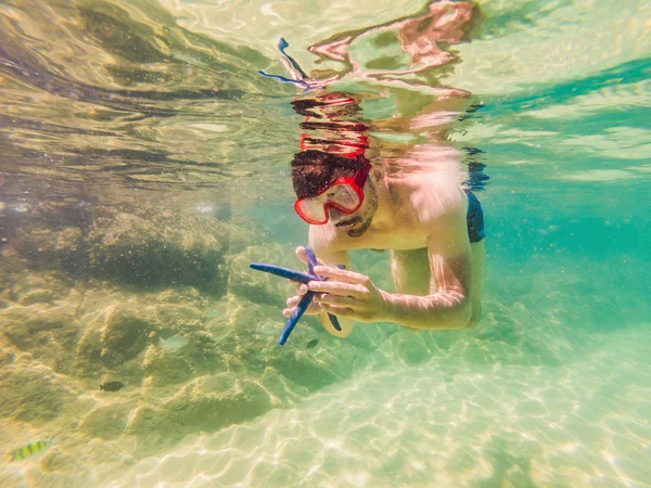 若い男性は、カラフルな魚や海洋生物との深い青色の海で水中サンゴ礁の風景の背景を探索シュノーケリング — ストック写真