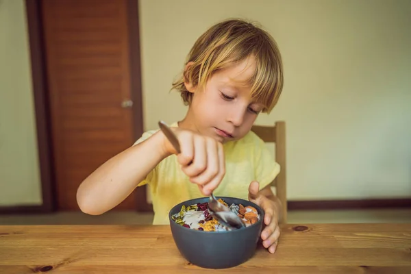 Niño feliz sentado y comiendo un tazón de batido fresco con mango, fruta de dragón, granola y semillas de chía —  Fotos de Stock