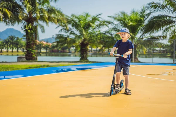 Šťastné dítě, že skútr na hřišti na basketbal. Děti se učí bruslit. Chlapeček bruslí za slunného letního dne. Venkovní aktivity pro děti na bezpečné obytné ulici. Aktivní sport — Stock fotografie