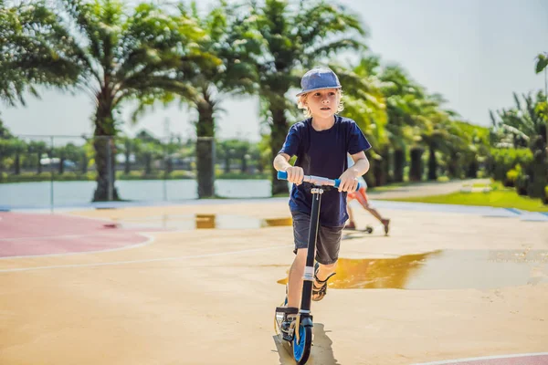 Счастливый ребенок на кик скутере на баскетбольной площадке. Дети учатся кататься на роликах. Маленький мальчик катается в солнечный летний день. Активный отдых для детей на улице. Активный спорт — стоковое фото