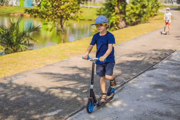 Bambino su scooter calcio nel parco. I bambini imparano a pattinare a rotelle. Ragazzino che pattina nella soleggiata giornata estiva. Attività all'aperto per bambini su strada residenziale sicura. Sport attivo per bambini in età prescolare — Foto Stock