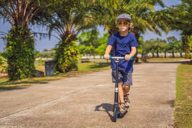 Çocuk Parkı tekme scooter üzerinde. Çocuklar paten silindir kuruluna öğrenin. Küçük çocuk güneşli yaz gününde pateni. Güvenli konut sokakta çocuklar için açık hava etkinliği. Okul öncesi çocuk için aktif spor