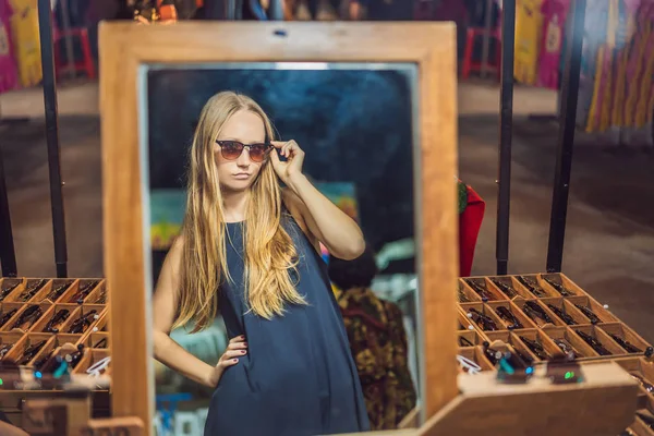 Young woman tourist trying on glasses on Walking street Asian market