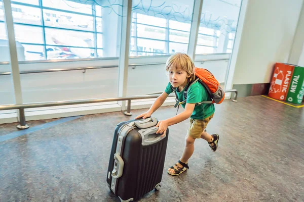 Lustiger kleiner Junge auf Urlaubsreise mit Koffer am Flughafen, drinnen — Stockfoto