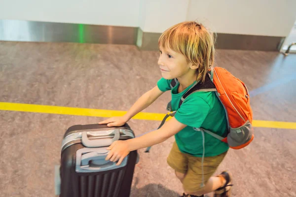 Śmieszne mały chłopiec będzie na wyjazd wakacje walizka na lotnisku, w pomieszczeniu — Zdjęcie stockowe