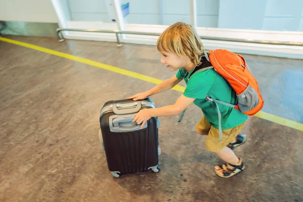 Lustiger kleiner Junge auf Urlaubsreise mit Koffer am Flughafen, drinnen — Stockfoto