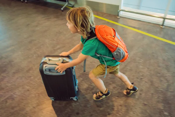 Lustiger kleiner Junge auf Urlaubsreise mit Koffer am Flughafen, drinnen — Stockfoto