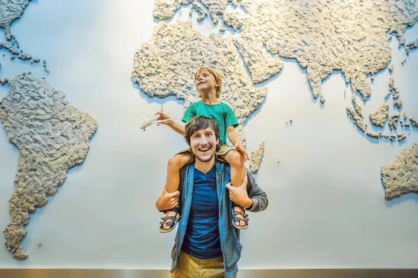 Ο μπαμπάς και ο γιος στο φόντο ενός παγκόσμιου χάρτη με ένα αεροπλάνο στα χέρια του. Σχέδιο ταξιδίου — Φωτογραφία Αρχείου