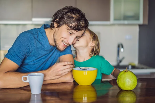 Pai e filho estão conversando e sorrindo enquanto tomam um café da manhã na cozinha — Fotografia de Stock