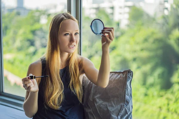 Mujer joven está aplicando maquillaje frente a la ventana en el apartamento estudio de belleza. Maquillaje profesional peinado. Tonalidad de piel. El color brillante componen con las pestañas largas y la piel fresca joven — Foto de Stock