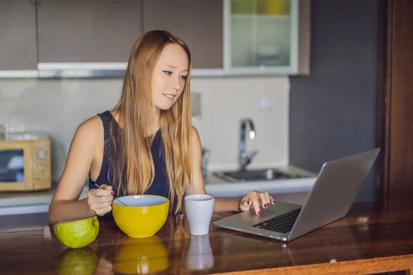 Beautiful woman having coffee and fruits for breakfast and looks into the laptop — Stock Photo, Image