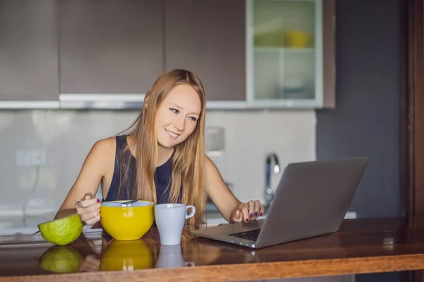 Beautiful woman having coffee and fruits for breakfast and looks into the laptop — Stock Photo, Image