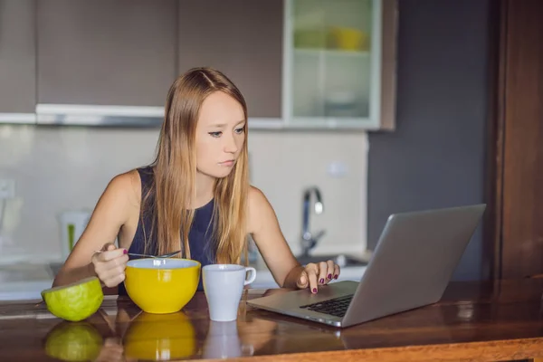 Beautiful woman having coffee and fruits for breakfast and looks into the laptop — Stock Photo, Image