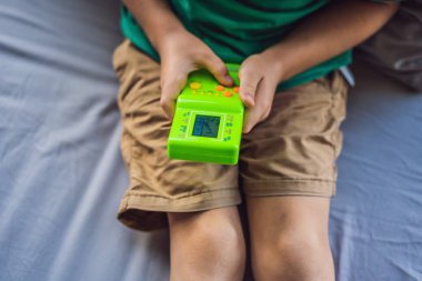 Tetris oynayan küçük bir çocuk. Eski okul taşınabilir oyun konsolu, tek renkli ekranlı elektronik eski cep oyuncağı