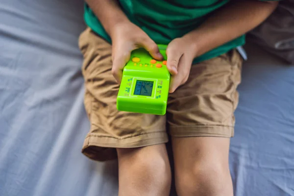 Tetris oynayan küçük bir çocuk. Eski okul taşınabilir oyun konsolu, tek renkli ekranlı elektronik eski cep oyuncağı — Stok fotoğraf