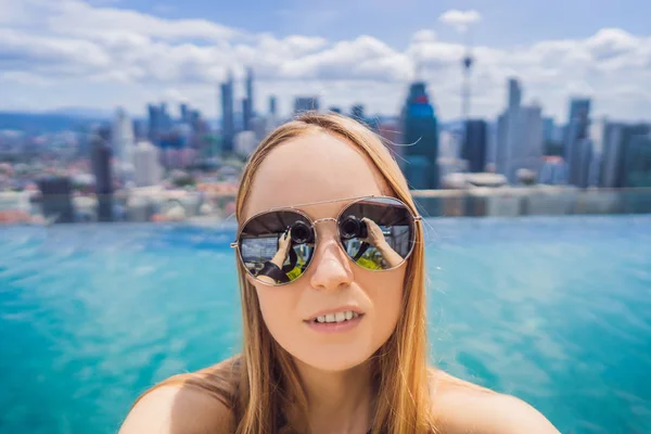 Młoda kobieta robi selfie w odkrytym basenie z widokiem na miasto na błękitne niebo. Bogaci ludzie — Zdjęcie stockowe