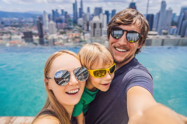 Vacaciones y tecnología. Familia feliz con niños tomando selfie juntos cerca de la piscina con vistas panorámicas de la ciudad — Foto de Stock