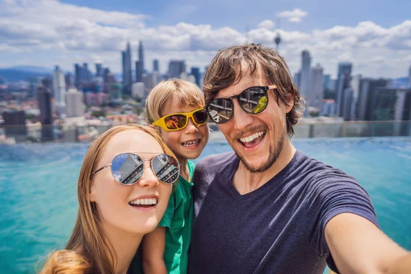 Vacaciones y tecnología. Familia feliz con niños tomando selfie juntos cerca de la piscina con vistas panorámicas de la ciudad — Foto de Stock