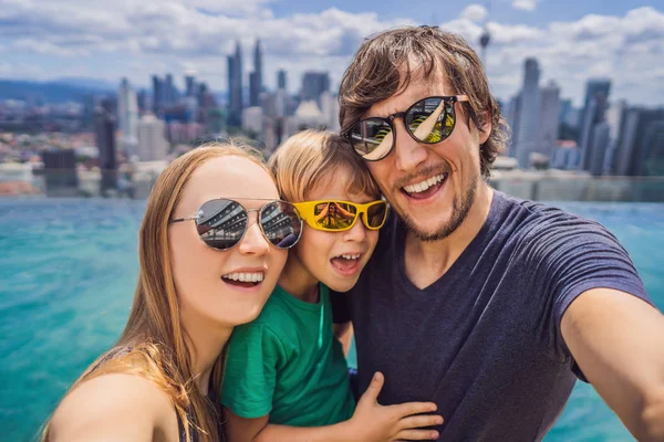 Vacaciones y tecnología. Familia feliz con niños tomando selfie juntos cerca de la piscina con vistas panorámicas de la ciudad — Foto de Stock