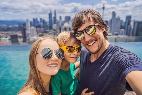 Vacaciones y tecnología. Familia feliz con niños tomando selfie juntos cerca de la piscina con vistas panorámicas de la ciudad — Foto de Stock