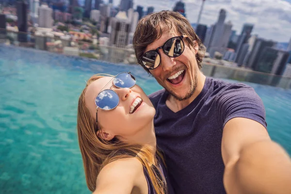 Joven feliz y atractiva pareja juguetona tomando foto selfie juntos en lujosa piscina infinita hotel urbano y vista panorámica de la ciudad disfrutando de vacaciones viaje de luna de miel en la diversidad étnica — Foto de Stock