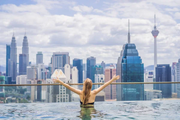 Mujer joven en la piscina al aire libre con vista a la ciudad en el cielo azul — Foto de Stock