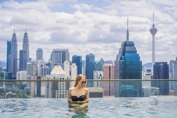 Mujer joven en la piscina al aire libre con vista a la ciudad en el cielo azul — Foto de Stock