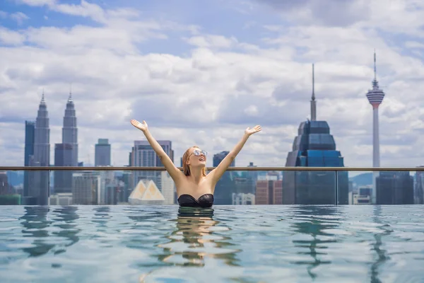 Mujer joven en la piscina al aire libre con vista a la ciudad en el cielo azul. Gente rica — Foto de Stock