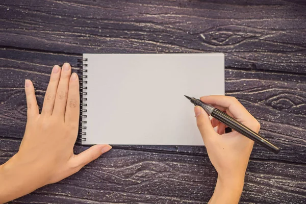 Vrouwen handen in een houten achtergrond met een bord, tekenblok, papier, mockup — Stockfoto