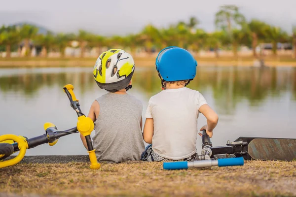 Два мальчика сидят на берегу озера после езды на велосипеде и скутере — стоковое фото